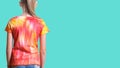 View from the back of a girl in a t-shirt in the style of tie dye on a turquoise background.