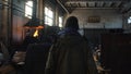 View from the back of man in protective coveralls and black cap going on the old steel making plant near melting furnace