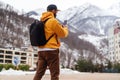 View from back. Man tourist in yellow hoodie, cap with backpack stands on background of high snowy mountains and using smartphone Royalty Free Stock Photo