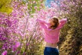 View from the back-slender attractive girl in pink clothes stands with her hands up among wild bushes covered with lilac flowers