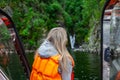 View from the back to the head of a beautiful young blonde girl in an orange life jacket sitting on the edge and looking far in a