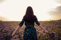 View from the back of a woman brunette with a bouquet of purple flowers on a flower field in the sunset, freedom, dreams