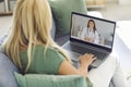 View from the back of a woman talking on a video call with her doctor sitting on the couch at home. Royalty Free Stock Photo