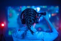 View from back of young emotional gamer woman with pigtail playing video game at home in front of big screen with headphone and