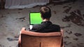 View from the back of young man in black shirt sitting in the brown comfortable chair and working on laptop computer