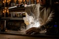 View of barman pouring steaming drink from shaker cup into wine glass