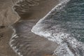 View of the beach with dark sand and the sea water, water with white foam and the effect of the sun reflecting in the water Royalty Free Stock Photo