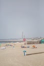 View at the beach with people taking sunbath on beach, lifeguard lifebuoys and a beach bar, lighthouse as background