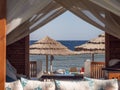 View Of A Beach Umbrella Made Of Straw And Blue Sky With The Ocean Or Sea Through The Window Of A Beach House. Beach Vacation And Royalty Free Stock Photo