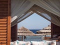 View Of A Beach Umbrella Made Of Straw And Blue Sky With The Ocean Or Sea Through The Window Of A Beach House. Beach Vacation And Royalty Free Stock Photo