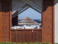 View Of A Beach Umbrella Made Of Straw And Blue Sky With The Ocean Or Sea Through The Window Of A Beach House. Beach Vacation And Royalty Free Stock Photo