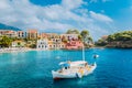 View of beautiful bay of Assos village with fishing boat at anchor in front and clouds in background, Kefalonia island Royalty Free Stock Photo