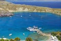 View on beautiful Lindos bay with white boats on water, cruise ships. Sand beach with swimming tourists. Blue crystal clear water