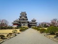 View of beautiful Matsumoto crow castle through entrance road with snow mountain and blue sky background during cherry blossom Royalty Free Stock Photo