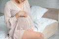 View of beautiful pregnant woman in nightie touching tummy in bedroom