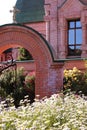 View of the beautiful, red-brick arch and forged fence, on the grounds of the crucified church, White daisies and roses grow Royalty Free Stock Photo