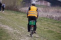 View from Behind of a Man on a Bicycle with a Reflective Jacket and a Green Basket Behind as a Luggage Carrier