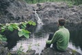 View from behind man hiker traveller sitting near mountain waterfall. Peaceful and calmness scenic view. Active person outdoor