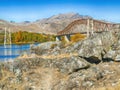 View from behind rocks of a lake and bridge over it with mountain and fall trees on the other side Royalty Free Stock Photo