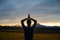 View from behind of a young woman meditating with her hands joined above her head outside