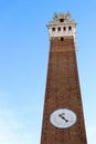 View from below to Mangia tower torre del Mangia, symbol of Siena, with clock on the winter blue sky background, Tuscany, Italy Royalty Free Stock Photo