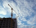 A view from below of an unfinished house and two construction cranes against the sky with white clouds. Construction Royalty Free Stock Photo
