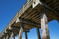 View from beneath an ocean pier, concrete pilings supporting wood pier deck and railings, silhouetted against a deep blue sky