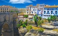 View beyond medieval stone bridge on ancient village on cliff top with cliffside restaurant, blue sky - Ronda, Spain