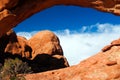 View beyond natural red sandstone arch bridge on rock against blue sky with clouds - Arches National Park, Utah Royalty Free Stock Photo