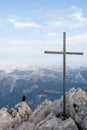 Black bird sitting next to a cross on top of a mountain Royalty Free Stock Photo