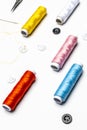 View of black and white buttons, needle with threaded yellow thread, various colors on thread spools on white background Royalty Free Stock Photo