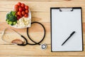 View of blank clipboard with pen near stethoscope and tasty vegetables on heart-shape plate Royalty Free Stock Photo