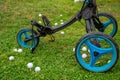 View of blue and black golf cart with three wheels, and white golf balls, on grass