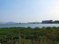 The view of blue calm sea with the green grass in the foreground, building in a far distance with mountains under the blue sky. Royalty Free Stock Photo