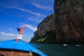 View on blue decorated wooden bow of longtail boat and rock wall under blue sky with few cirrus clouds Royalty Free Stock Photo