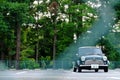 View of a blue Mini Cooper parked before the trees