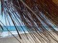 View of the blue sea with salt water through the yellow dry straw of the sun umbrella on the beach in the warm eastern tropical Royalty Free Stock Photo