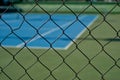view of a blue synthetic tennis court through a fence