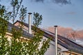 View between blurred bushes to two stainless steel chimneys and roofs with solar panels in the light of dusk