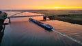 View of A boat sailing beneath a bridge on the riverbank, the sun setting in the background