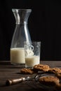 View of bottle and glass of milk on wooden table with chocolate chip cookie, selective focus, black background, vertical Royalty Free Stock Photo