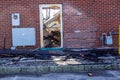 View through a broken glass door on a brick wall showing burnt debris after a store fire. There are also charred building..