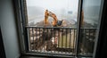 View from a building window overlooking a muddy construction site with a large excavator Royalty Free Stock Photo