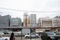 View of buildings, cars, electric cables and a bridge in a city on a cloudy day