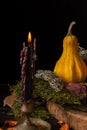 View of burning black candle with yellow pumpkin and autumn leaves, black background, vertical