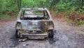 View burnt out and rusty car wreck alongside road and woods Royalty Free Stock Photo
