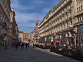 View of busy shopping street Graben in the historic center of Vienna, Austria on sunny day with Plague Column, cafe and people.