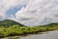 View from the calm river on green trees and bushes against the background of high rocky mountains in the middle of a sunny day. Royalty Free Stock Photo