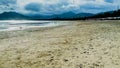 View of a calm stretch of sand beach without people and calm waves against a backdrop of mountains and blue sky