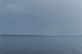 view of the calm undulating blue water of Lake Baikal, mountains on horizon, gray sky, shower, rain